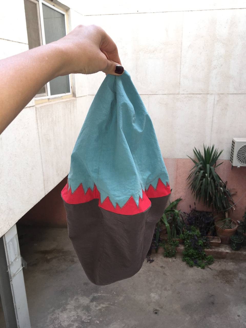 Hand holding up a turquoise and brown hat in the courtyard
