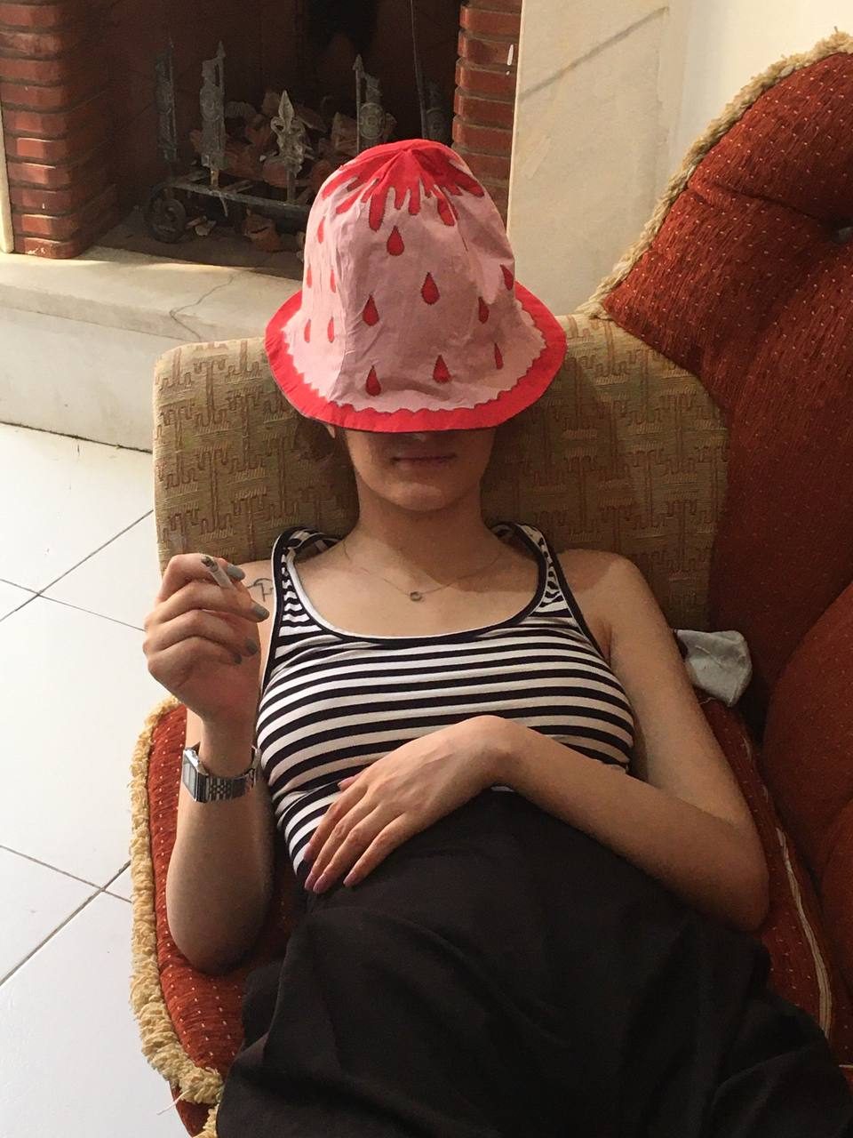 Model relaxing in an armchair with a pink hat tipped over the face