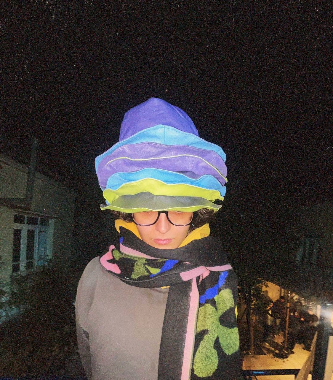 Model at night wearing a tall stack of colourful hats