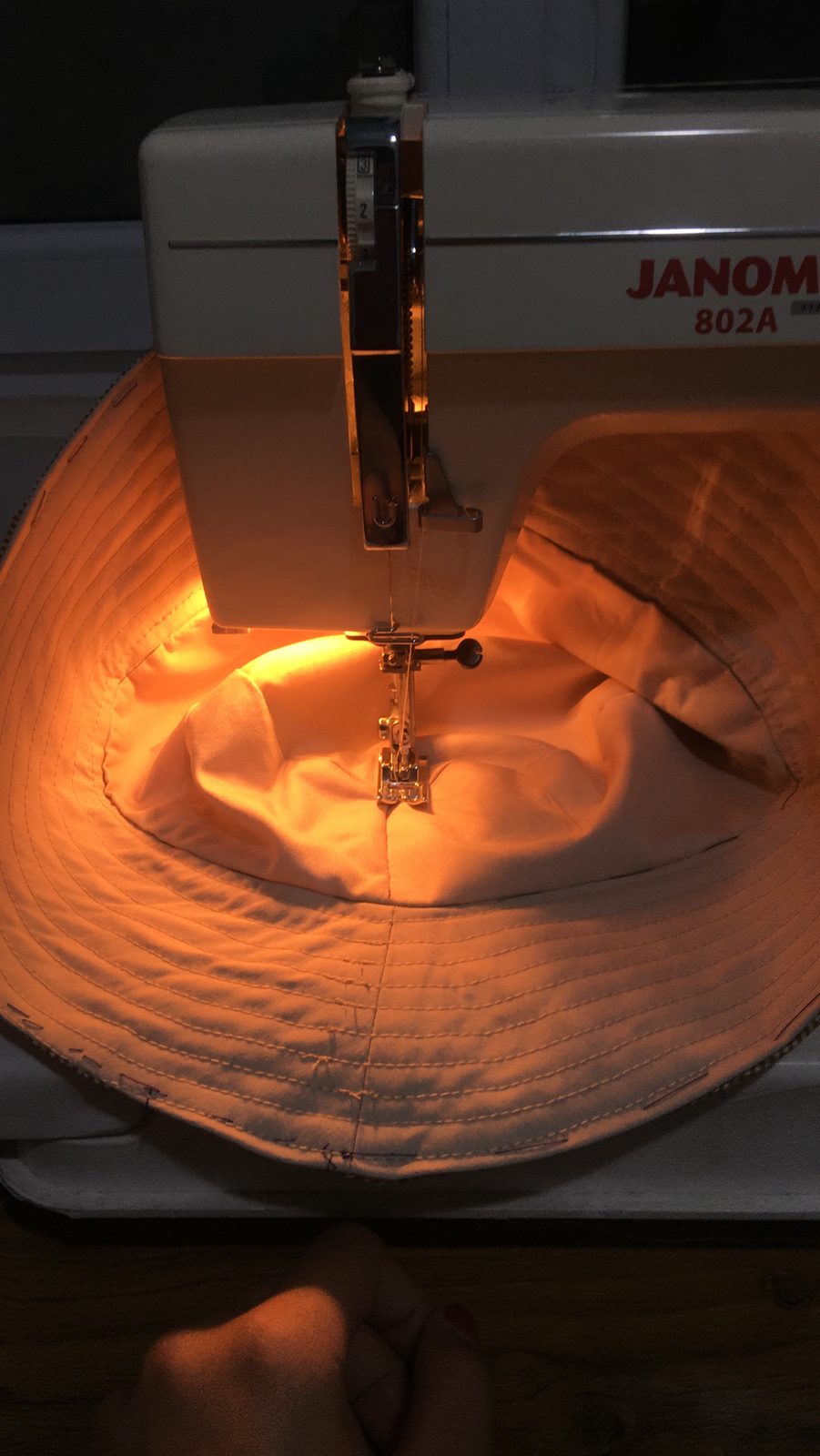Sewing machine needle lit in warm amber light while stitching a hat