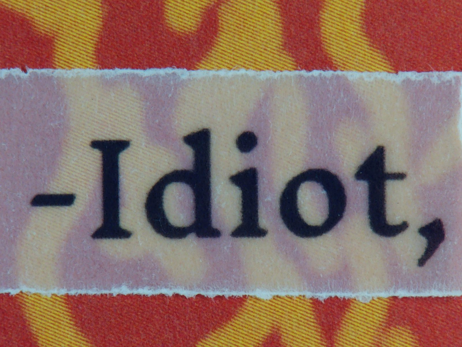 Red and yellow flame-patterned page with torn text reading Idiot