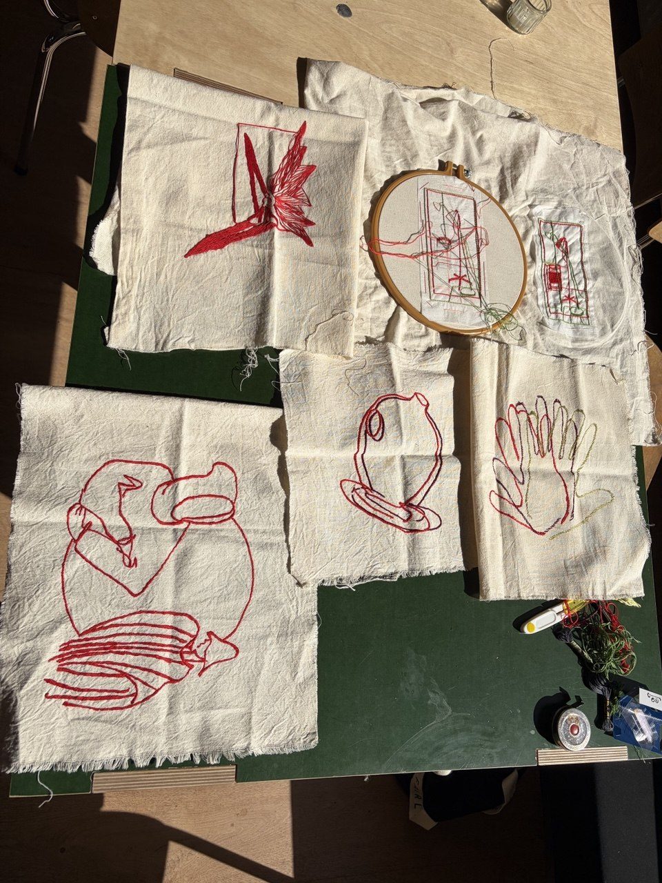 Embroidery hoop and red-thread drawings on white cloth
