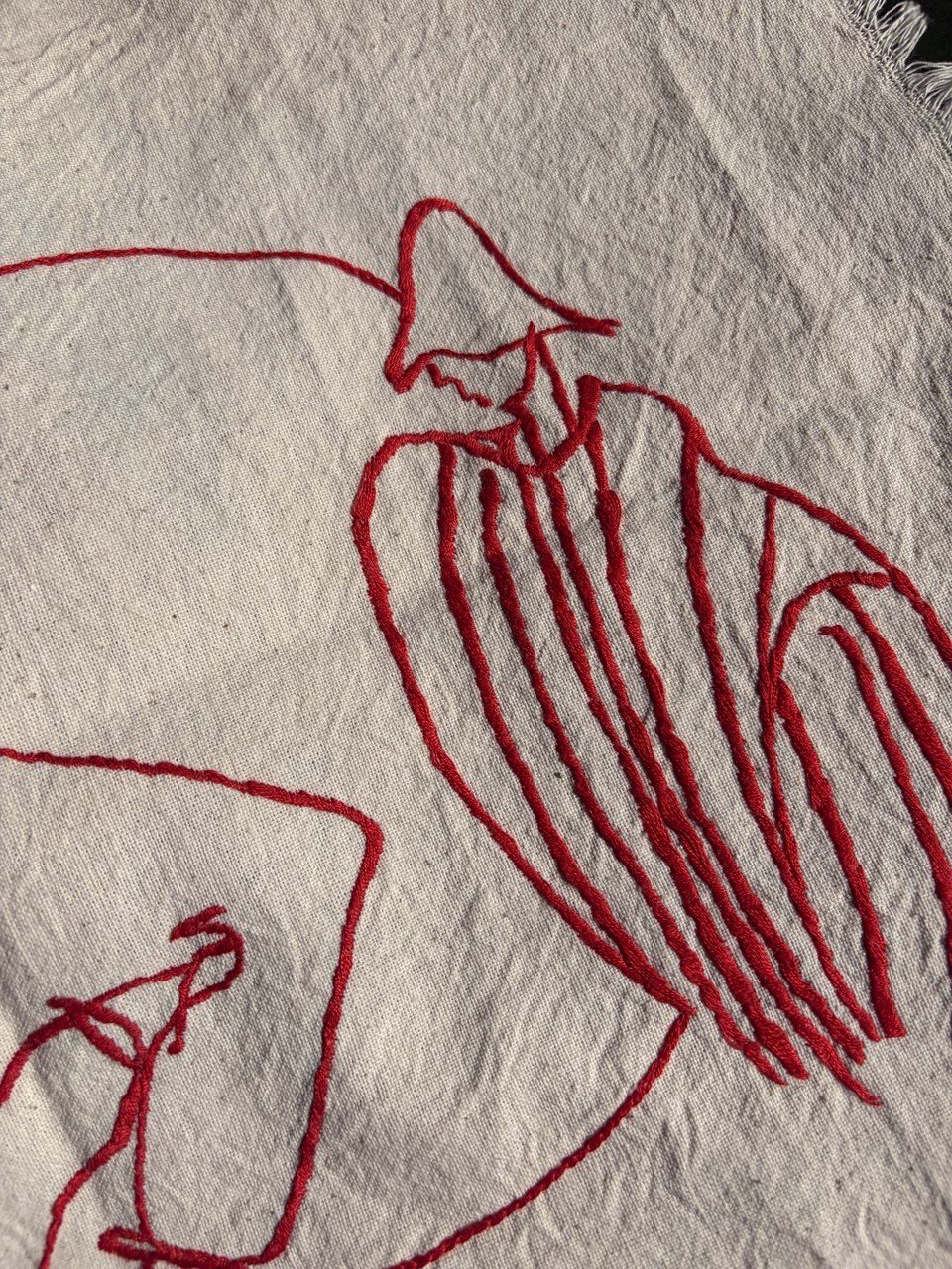 Close-up of a figure embroidered in red thread on white cloth